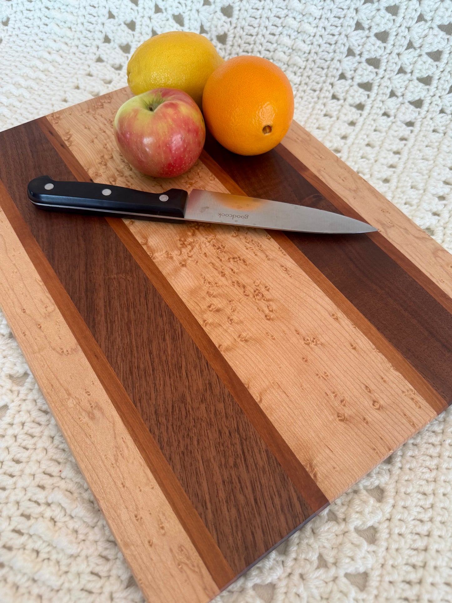 Close up Birdseye, BlackWalnut, and Cherry 12x16 cutting board with fruits and knife. 