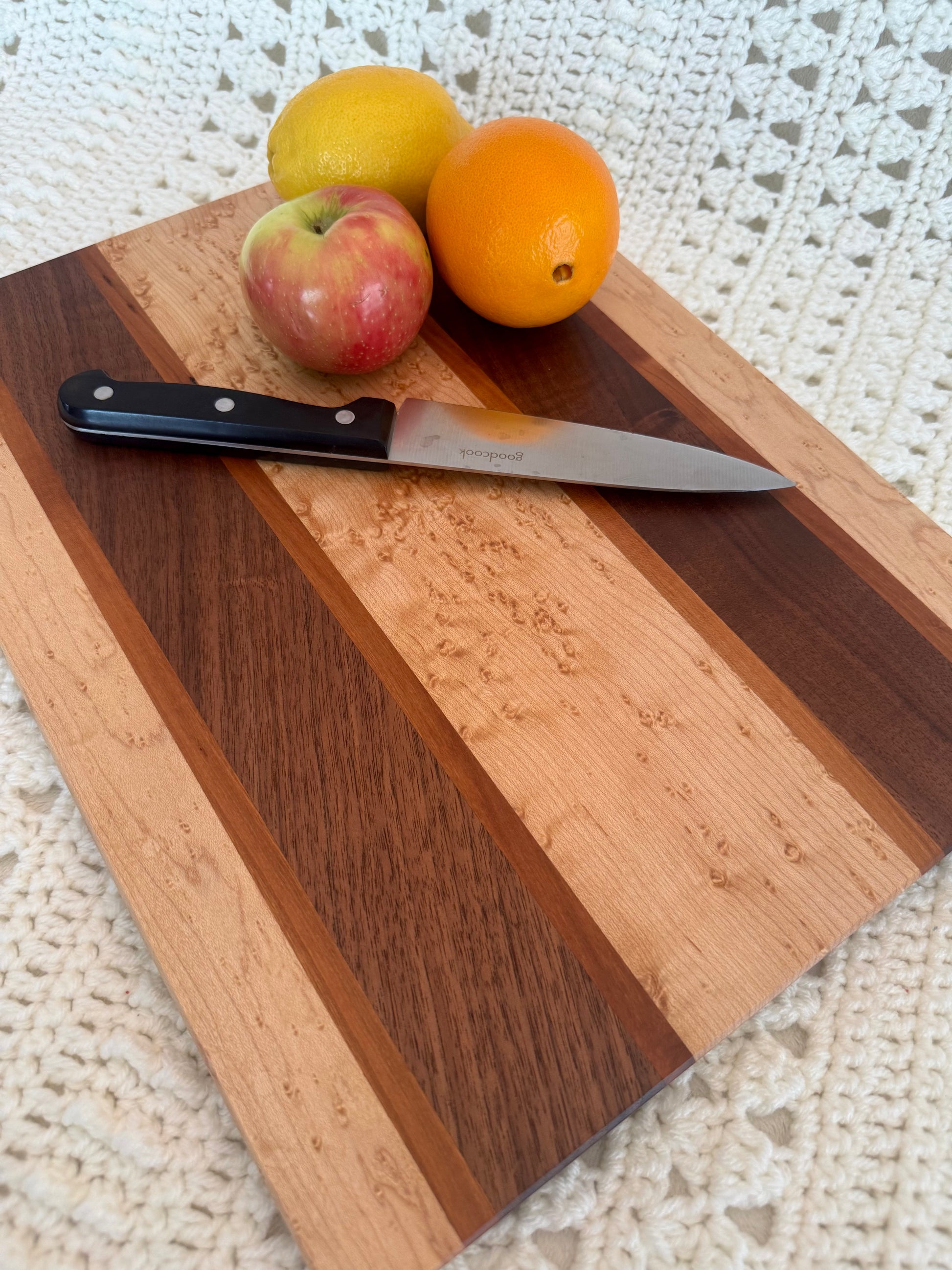 Close up Birdseye, BlackWalnut, and Cherry 12x16 cutting board with fruits and knife. 
